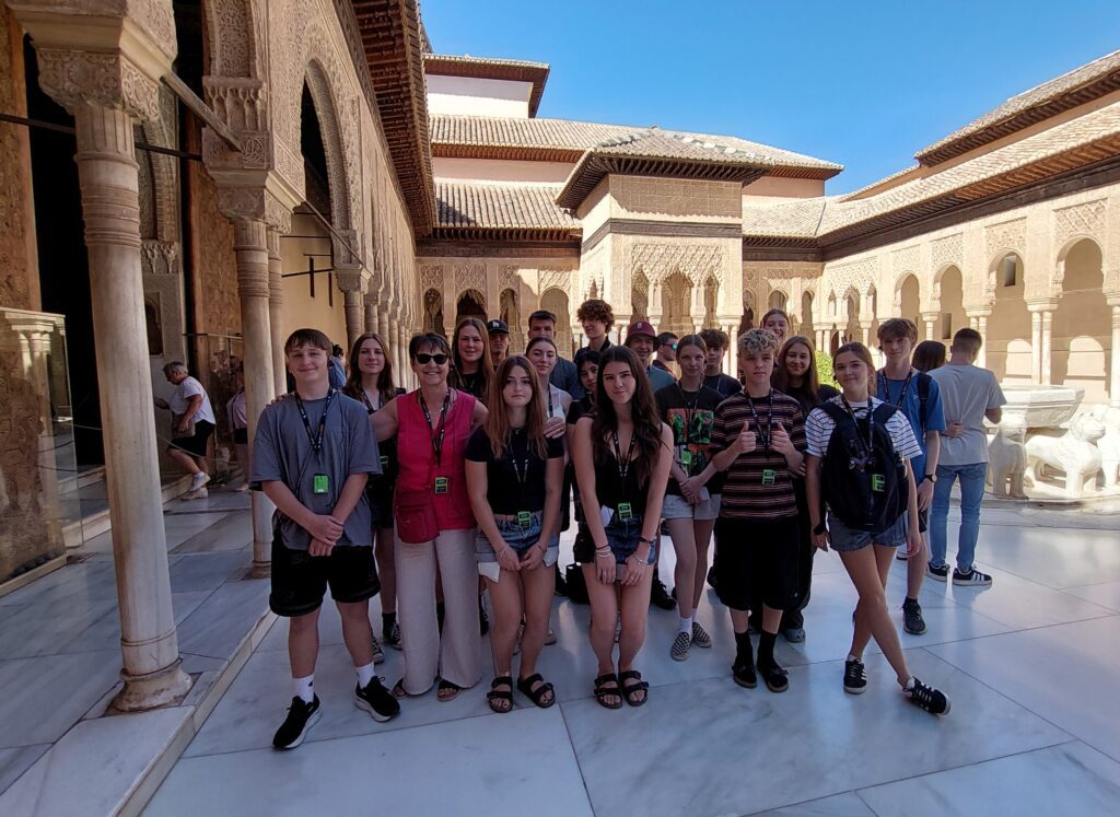 Une enseignante et son groupe d'élèves souriants lors d'un séjour éducatif au Patio des Lions de l'Alhambra à Grenade.